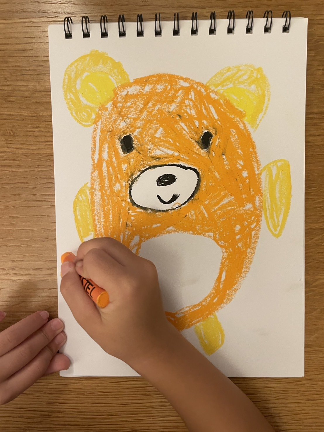 クレヨンでクマの塗り絵を楽しんでいるお子さんの手元